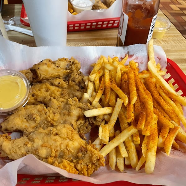 A red basket holds fried chicken tenders, seasoned fries, and a side of honey mustard.