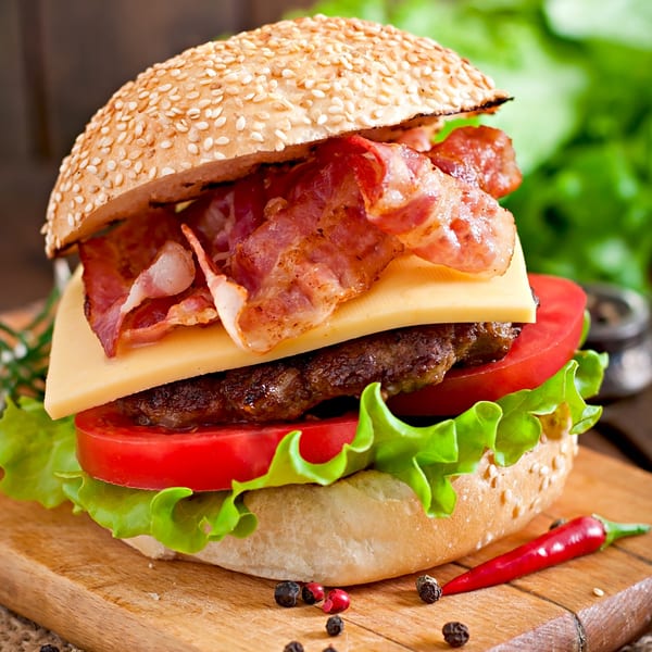 A gourmet Insomnia Steak & Grill burger with bacon, cheese, tomato, and lettuce on a sesame bun.
