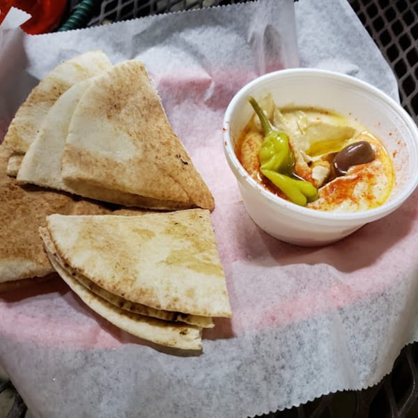 Mediterranean hummus with olives and peppers, served with pita bread on a white paper-lined basket.