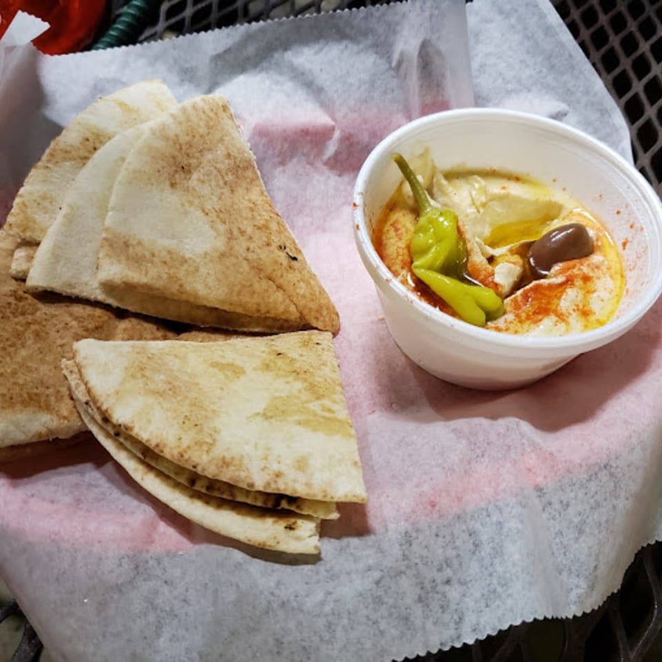 Mediterranean hummus with olives and peppers, served with pita bread on a white paper-lined basket.